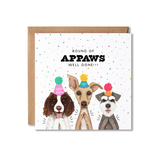 A square greeting card with a kraft envelope behind it, featuring three illustrated dogs wearing party hats and the text 'ROUND OF APPAWS WELL DONE!!!' on a white background with scattered confetti.