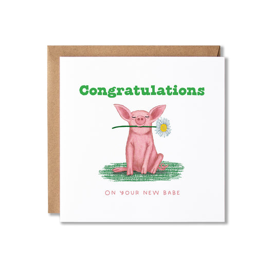 A square congratulations card with a kraft envelope behind it. The card features a watercolor-style pink pig sitting on green grass and holding a daisy in its mouth, with the text 'Congratulations' in green and 'ON YOUR NEW BABE' in pink.