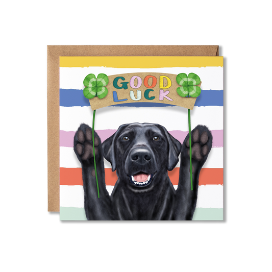 Greeting card with a black Labrador dog holding four-leaf clovers and 'Good Luck' sign on striped background