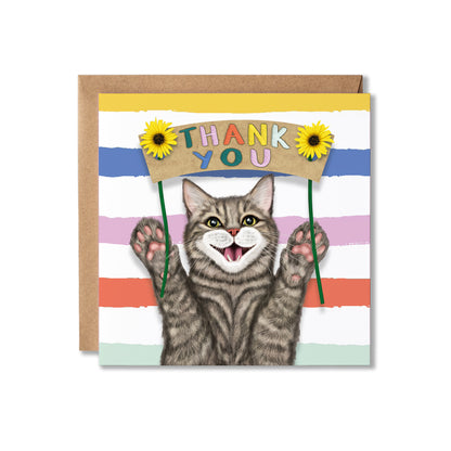 A square greeting card with a brown kraft envelope behind it. The card features a smiling gray tabby cat holding a cardboard sign that says 'THANK YOU' in colourful letters, with yellow sunflowers on either side.