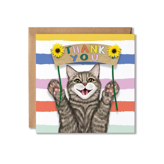 A square greeting card with a brown kraft envelope behind it. The card features a smiling gray tabby cat holding a cardboard sign that says 'THANK YOU' in colourful letters, with yellow sunflowers on either side.
