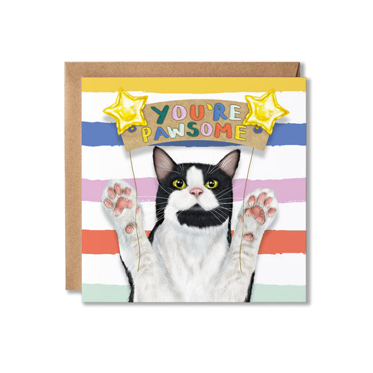 A square greeting card featuring a black-and-white cat with paws raised, holding a banner that reads 'YOU'RE PAWSOME,' set against pastel horizontal stripes. A brown kraft envelope is placed behind the card on a white background.