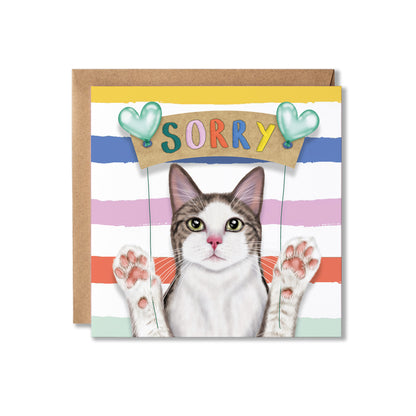 A square greeting card with a brown kraft envelope behind it. The card features a cat illustration with raised paws under a sign that says 'SORRY' in colourful letters, with pastel horizontal stripes in blue, pink, orange, and mint.