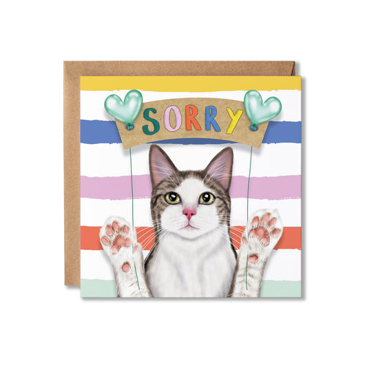A square greeting card with a brown kraft envelope behind it. The card features a cat illustration with raised paws under a sign that says 'SORRY' in colourful letters, with pastel horizontal stripes in blue, pink, orange, and mint.