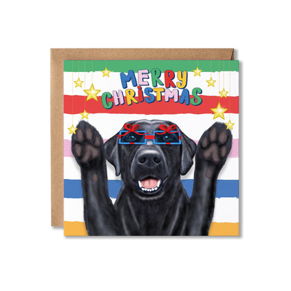 A square Christmas greeting card featuring a black dog wearing present shaped glasses and raising its paws, with the text 'MERRY CHRISTMAS' in colorful letters. The card has a striped background and is shown with a brown kraft envelope.