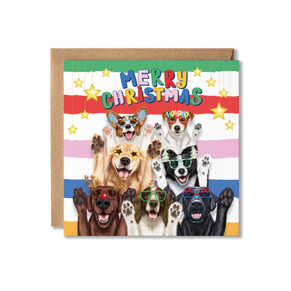 A square Christmas greeting card with a kraft envelope behind it. The card features the text 'MERRY CHRISTMAS' in colourful letters above a group of seven dogs wearing funny Christmas sunglasses, set against a striped background with gold stars.