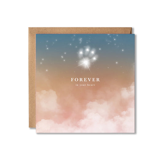 A square greeting card with a kraft envelope, featuring a dreamy sky design with blue and pink clouds, white stars in the shape of a paw print, and the text 'FOREVER in your heart'.