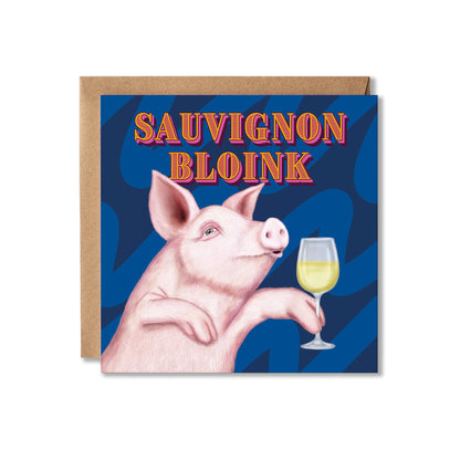 A square greeting card with a kraft envelope behind it, featuring an illustration of a pink pig holding a glass of white wine against a dark blue patterned background, with the text 'SAUVIGNON BLOINK' in orange and yellow.