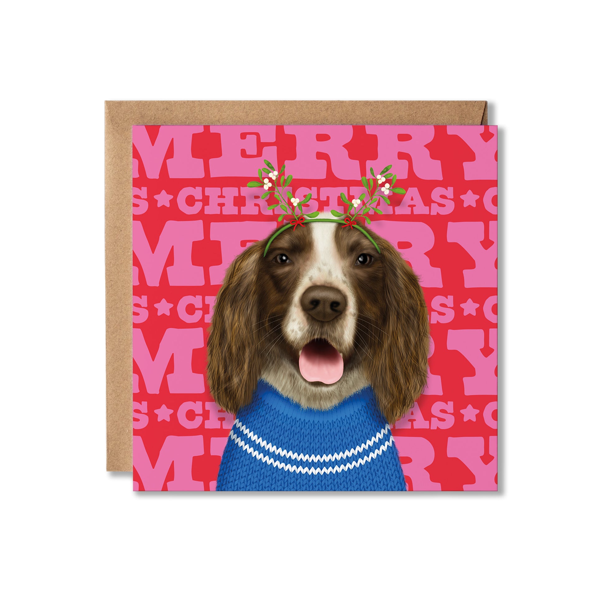 A square Christmas greeting card featuring a brown and white dog wearing a blue sweater and a green holly leaf crown, set against a red background with pink 'MERRY CHRISTMAS' lettering. A brown kraft envelope is placed behind the card on a white background.
