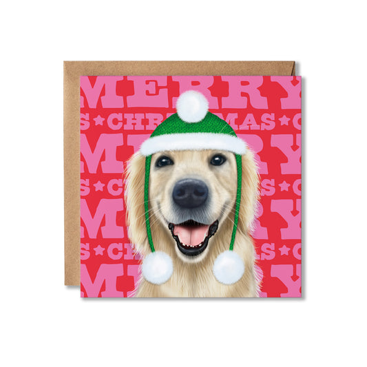 A square Christmas greeting card featuring a Golden Retriever dog wearing a green Santa hat with white pom-poms, set against a pink and red patterned background with the word 'MERRY CHRISTMAS' repeated. A brown kraft envelope is placed behind the card on a white background.