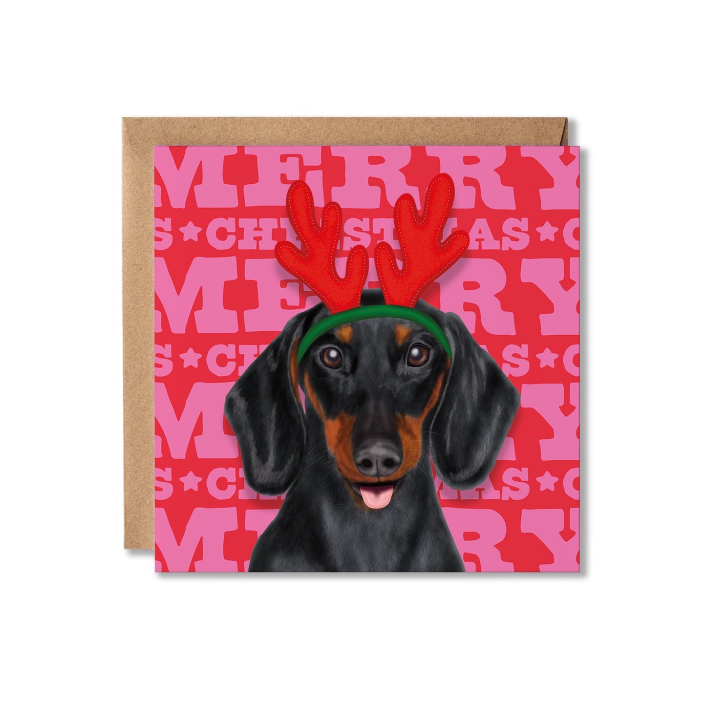 A square Christmas greeting card featuring a black and tan dachshund wearing red reindeer antlers and a green headband, set against a pink and red Merry Christmas background. A brown kraft envelope is partially visible behind the card on a white background.