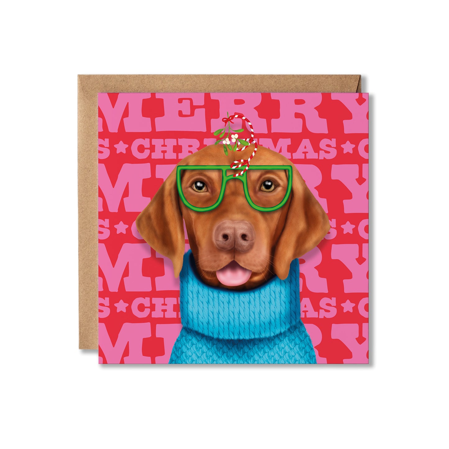A square Christmas greeting card featuring a brown dog wearing green glasses, a blue knit sweater, and a candy cane on its head, set against a pink patterned background with the words 'MERRY CHRISTMAS.' A kraft envelope is placed behind the card on a white background.