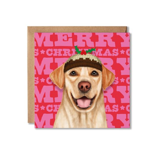 A square Christmas greeting card featuring an illustration of a yellow Labrador retriever wearing a brown knit Santa hat with green holly leaves, set against a pink and red background with repeating 'MERRY CHRISTMAS' text. A brown kraft envelope is placed behind the card on a white background.