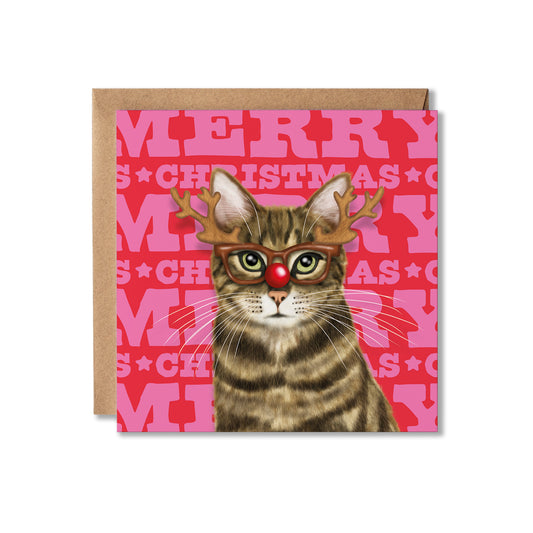 A square Christmas greeting card featuring a tabby cat wearing glasses with antlers and a red nose, set against a pink background with repeated 'MERRY CHRISTMAS' text. A kraft paper envelope is placed behind the card on a white background.