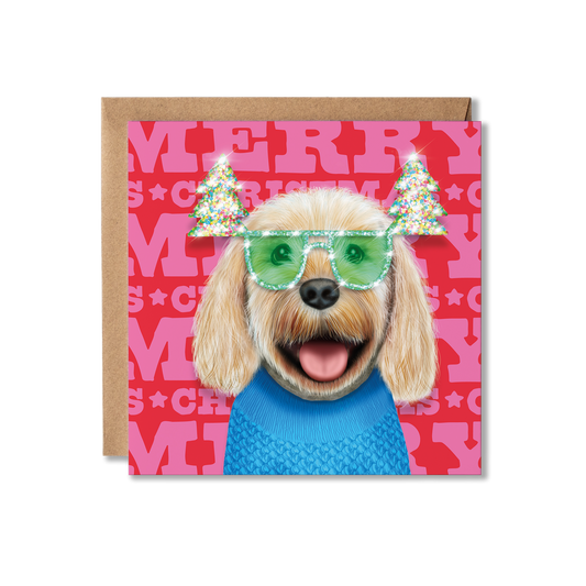 A cream cockerpoo dog in a blue knitted jumper and green Christmas tree glasses with a Merry Christmas background