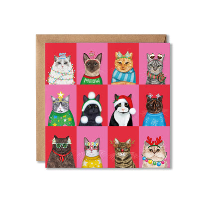 A square greeting card with a brown envelope behind it, featuring a grid of 12 illustrated cats wearing colorful Christmas hats, scarves, and accessories on pink and red backgrounds.